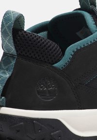 Zapatilla negra con parte superior texturizada, acentos en teal contrastantes, detalles de malla y una entresuela blanca con una suela exterior negra texturizada.