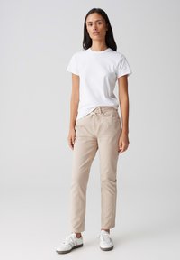 Witte T-shirt met korte mouwen, gecombineerd met lichtbeige tapse broek en witte sneakers; casual outfit met een eenvoudig ontwerp en geen zichtbare patronen.