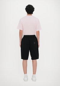 Light pink short-sleeve t-shirt and black knee-length shorts with an elastic waistband, featuring a small logo detail on the shorts.