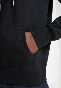 Felpa nera con tasca canadese frontale, polsini e orlo a costine, caratterizzata da una texture liscia e cuciture a contrasto.