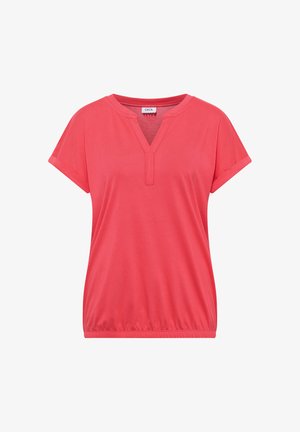 Kvinde set fra ryggen iført en koralfarvet t-shirt med korte ærmer og lyseblå jeans mod en ensfarvet hvid baggrund.