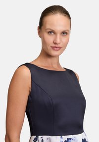 Navy Satin Kleid mit ärmellosem Design, Rundhalsausschnitt und gemustertem Rock mit blauen Blumenakzenten. Glatte Textur insgesamt.