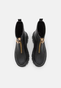 Musta nahkaiset nilkkurit, joissa on paksu pohja, kultaiset vetoketj yksityiskohdat ja vetotappu helppoa pukemista varten. Tasainen pinta ja rakenteellinen muotoilu.