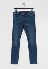 Blå denimjeans med rak benprofil och subtila slitageeffekter. De har fem fickor och en kontrasterande röd etikett i midjan.