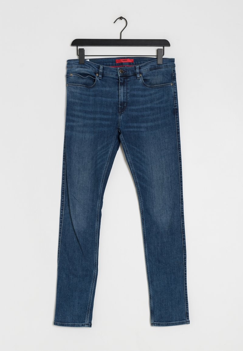 Blå denimjeans med rak benprofil och subtila slitageeffekter. De har fem fickor och en kontrasterande röd etikett i midjan.