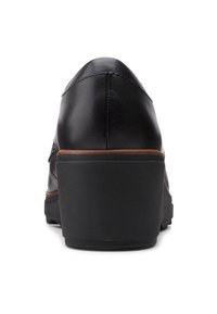Chaussure à talon compensé en cuir noir vue de dos avec une bordure marron au-dessus de la semelle épaisse.