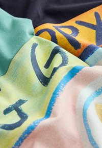 Kolorowa tkanina z literami w stylu blokowym w czerni, zawierająca fragmenty słowa "STORY", na zielonym, żółtym, pomarańczowym, różowym i niebieskim tle.