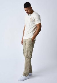 Crème t-shirt met een kleine grafische afbeelding op de borst, gecombineerd met lichte kaki cargo broeken met meerdere zakken en stikdetails.