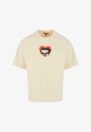 Krém színű pamut póló, laza szabású. Középen elhelyezett grafika két arcot ábrázol szív alakban, fekete kontúrokkal és élénk színekkel.