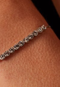 Zilveren armband met een rij van ronde heldere edelstenen, dicht op elkaar gezet op een gestructureerd huidoppervlak. Eenvoudig, elegant ontwerp.