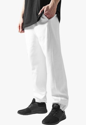 White sweatpants made of soft fabric, featuring an elastic waistband and cuffed ankles, worn with black athletic shoes.
