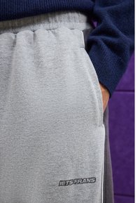 Grå bomulls joggebukser med elastisk midje, sidelommer og svart logo-akcent. Teksturen er jevn og litt børstet.