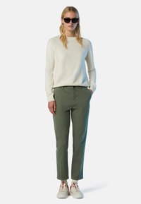 Helle Cremefarbenes Sweater, grüne maßgeschneiderte Hose und weiße Sneaker mit roten Akzenten. Das Outfit zeichnet sich durch ein minimalistisches Design mit einer schlanken Silhouette aus.
