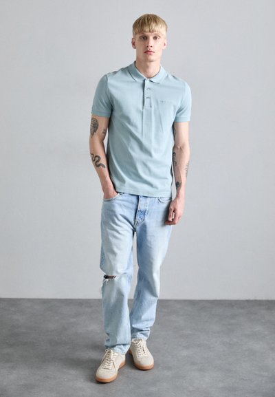 Svijetloplava pamučna polo majica kratkih rukava s tri gumba, u paru s svijetlosivim iznošenim trapericama i bež tenisicama.