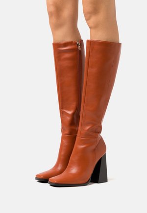 Bottes orange en cuir montant jusqu'au genou, avec un bout pointu, un talon carré et une fermeture éclair latérale. Texture lisse avec un design de tige ajustée.