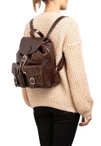 Bruine leren rugzak met een rond flap, voorste zakken met gespen en verstelbare banden. Gelaagde afwerking met een glanzend uiterlijk.