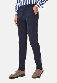 Chino navy in cotone con design a gamba dritta, dotati di tasche anteriori e chiusura a bottone. Abbinati a scarpe in suede marroni.
