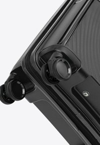 Black suitcase corner with smooth texture, featuring two rotating wheels and a zipper closure. Surface has linear grooves for design.