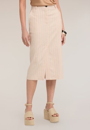 Beige high-waisted midi-rok met dunne verticale strepen en een voorste split, gedragen met plateau enkellaarsjes en armbanden.