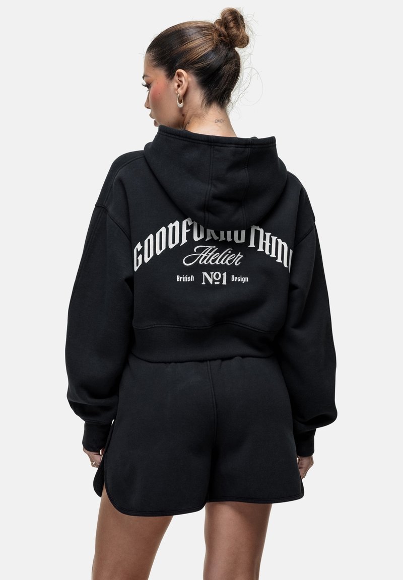 Felpa nera corta con un grande logo bianco sulla schiena e pantaloni corti neri abbinati. Il tessuto sembra morbido con una vestibilità comoda.