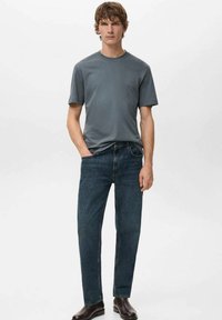 Harmaa lyhythihainen t-paita yhdistetty tummiin farkkuihin. Farkuissa on klassinen istuvuus ja suora lahje, vähäisillä metalliosilla.