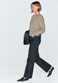 Maglione beige e jeans a gamba larga blu scuro, abbinati a scarpe nere a punta senza lacci. La donna porta una borsa nera con texture.