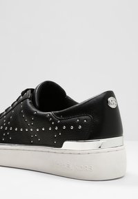 Černé kožené tenisky se stříbrnými hroty, zaobleného tvaru a bílé gumové podrážky. Obsahují akcent s logem a kovový detail na patě.