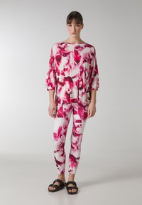 Blomstret top og leggings sæt i pink og hvid. Toppen har en løstsiddende pasform og brede ærmer; leggings er tætsiddende. Sorte sandaler.