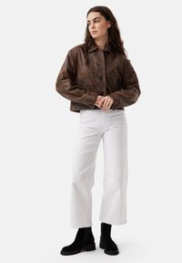 Brown leather cropped jacket with a button closure and two side pockets, paired with white wide-leg pants and black ankle boots.
