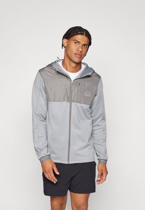 Chaqueta gris con cremallera y capucha, que presenta un panel gris más claro en el pecho. Textura de tela suave y detalle del logo en el lado izquierdo.