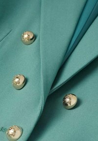 Tessuto turchese con una texture liscia, caratterizzato da tre bottoni metallici con una finitura testurizzata sul lato sinistro e un bordo piegato.