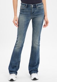 Jeans de campana azul en un lavado medio con desvanecimiento sutil. Presenta cinco bolsillos, cierre de botón de metal y pasadores para cinturón. Textura de mezclilla suave.