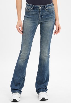 Jeans de campana azul en un lavado medio con desvanecimiento sutil. Presenta cinco bolsillos, cierre de botón de metal y pasadores para cinturón. Textura de mezclilla suave.