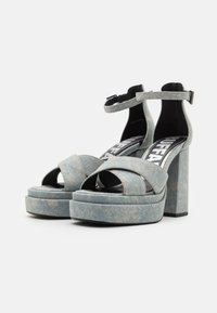 Denim-tyyliset korkeat sandaalit, joissa on paksu lohkokorko, ristikkäiset hihnat ja säädettävä nilkkahihna vaaleansinisessä värissä, erottuvalla ompeleella.