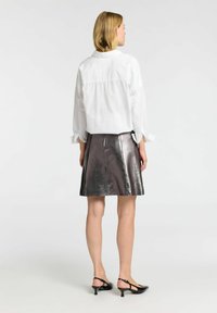 Hvid, langærmet skjorte med løs pasform og opholdte manchetter, parret med en metalskinnende sølv A-linje nederdel. Sorte slingback hæle fuldender looket.