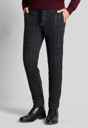 Schwarze karierte Hosen mit einem Kordelzugbund und seitlichen Taschen, kombiniert mit schwarzen Lederstiefeln. Glatter Stoff mit einer subtilen Textur.