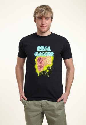 Czarna koszulka bawełniana z żywym neonowym nadrukiem, na którym widnieje napis "PRAWdziWY GRACZ" nad stylizowanym kontrolerem do gier, z efektem rozbryzgów.
