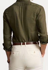 Olijfgroen linnen shirt met opgerolde mouwen, rugpand en knoopsluiting, gecombineerd met crèmekleurige broek en een bruine leren riem.