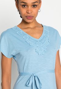 Vestido azul claro com decote em V, apresentando detalhes em renda intrincados, mangas curtas e um cinto na cintura para um ajuste ajustável.