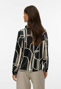 Sort og creme mønstret bluse med lange ærmer, prydet med geometriske designs og en glat, blank tekstur. Knappede manchetter fuldender udseendet.