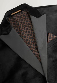 Zwarte fluwelen blazer met grijze revers, met een gevoerd interieur in een zwart en bruin geometrisch patroon, compleet met een pochet.