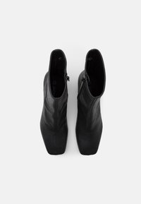 Botas de cuero negras hasta el tobillo con un diseño elegante, punta afilada y cremalleras laterales. Textura suave con una estética minimalista y sin elementos metálicos visibles.