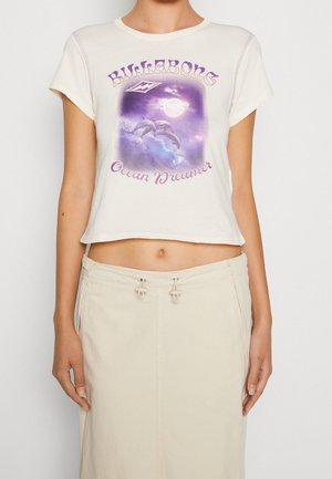 Top court crème présentant un graphique de dauphins sur un fond violet et bleu. Texte "Ocean Dreamer" en dessous du design. Manches courtes.