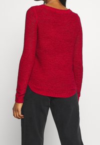 Maglione rosso a maglia con maniche lunghe, caratterizzato da un orlo a coste e una finitura leggermente texturizzata. Il retro ha un collo arrotondato e spacchi laterali.