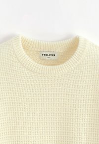Pull en maille couleur crème avec un col ras du cou côtelé, présentant un motif texturé. L'étiquette de la marque indique "FRILIVIN, taille M."