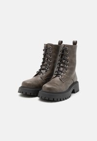 Brune lær ankle boots med tykke gummisåler, runde tær og sorte snørebånd. Metal øjer og hængsler er synlige øverst.