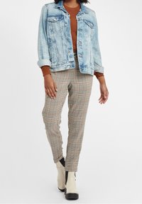 Denimjacka i ljusblått med två bröstfickor, kombinerad med en brun stickad tröja och beige rutiga byxor. Vita stövlar med svarta detaljer.