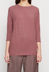 Maglietta a maniche lunghe color bordeaux realizzata in un tessuto morbido e strutturato con scollatura a girocollo. Presenta una vestibilità ampia e spacchi laterali all'orlo per facilitare i movimenti.
