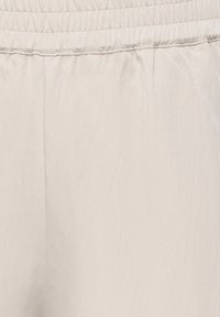 Tissu beige clair avec une taille élastique, montrant la texture et les détails des coutures.