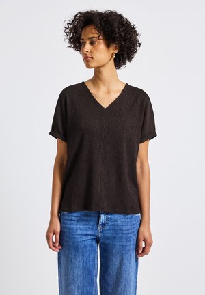 Brown short-sleeved V-neck top in a textured fabric, paired with light blue wide-leg jeans. Simple design with rolled sleeves.